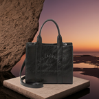 Black leather handbag with brand logo on a stone platform against a sunset ocean backdrop