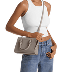 Person wearing a white tank top and blue jeans holding a gray handbag.
